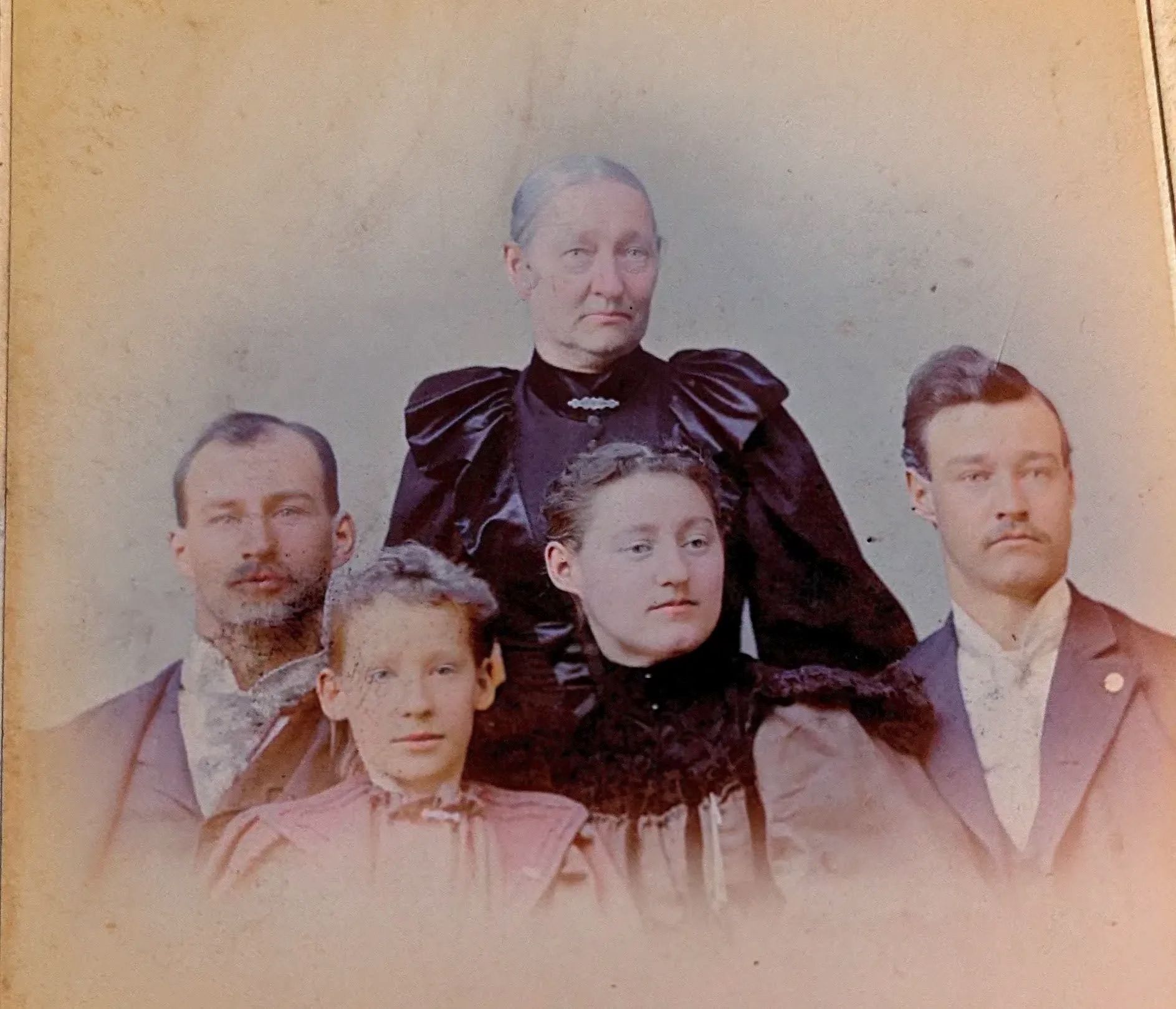 Photo of a family dressed in 1890s attire, suits on two men, dresses on 2 women and a young girl.