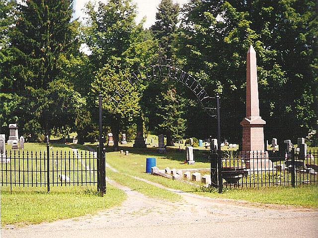 tall arched wrought iron gate with name LEE VALLEY at the top stands in front of a cemetery