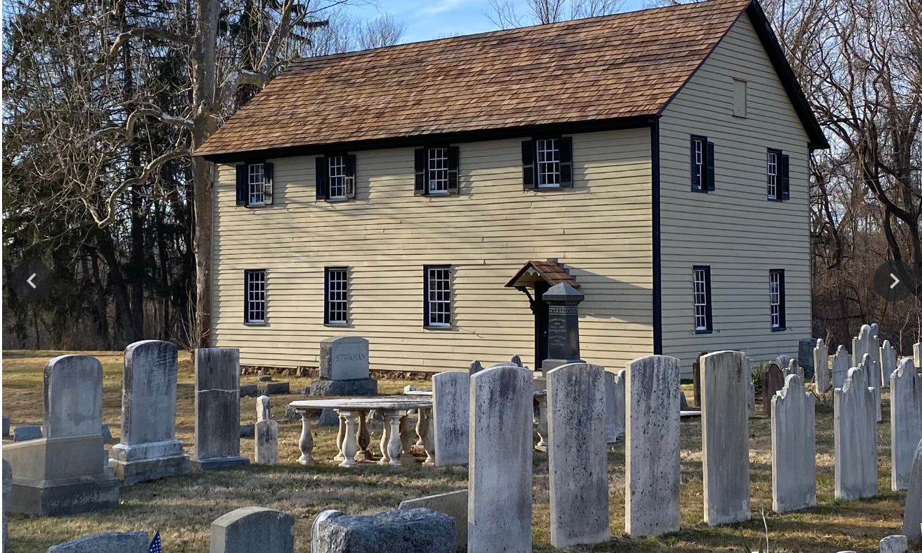 two story wooden house stands beside a cemetery