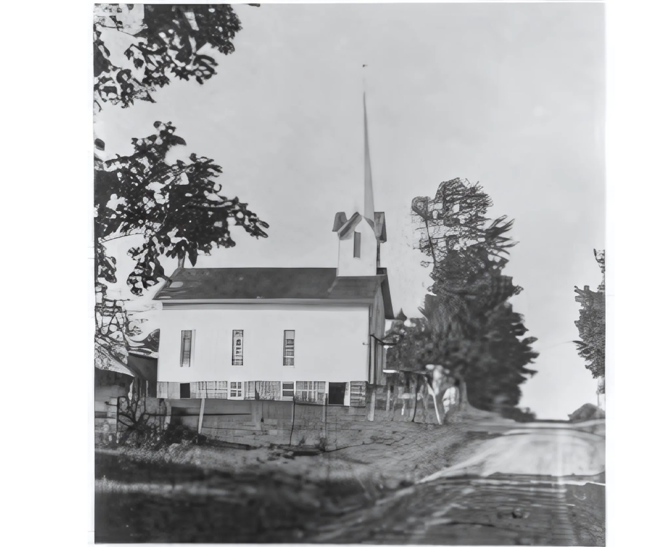 wooden white church on concrete foundation with tall steeple stands along a dirt road
