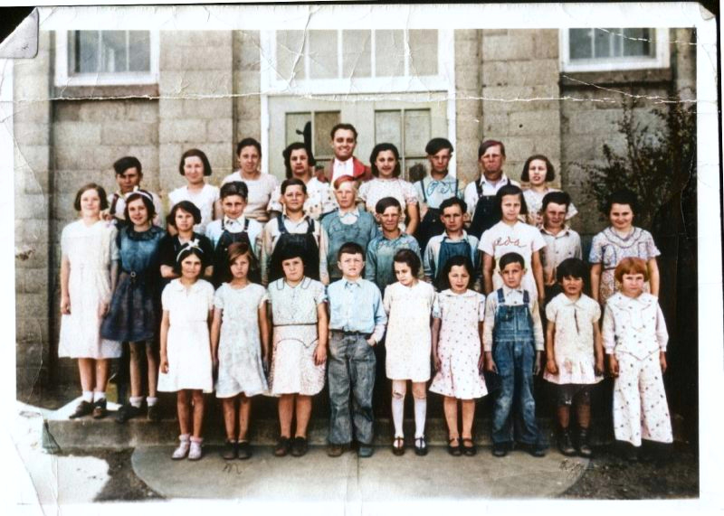 class photo taken outdoors in front of a masonry school building, children of ages approx 10-14
