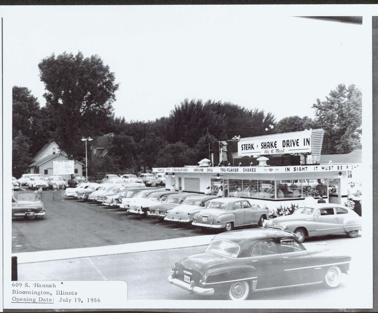 1950s style cars lined up in parking lot of drive up restaurant with marquis reading Steak and Shake Drive In